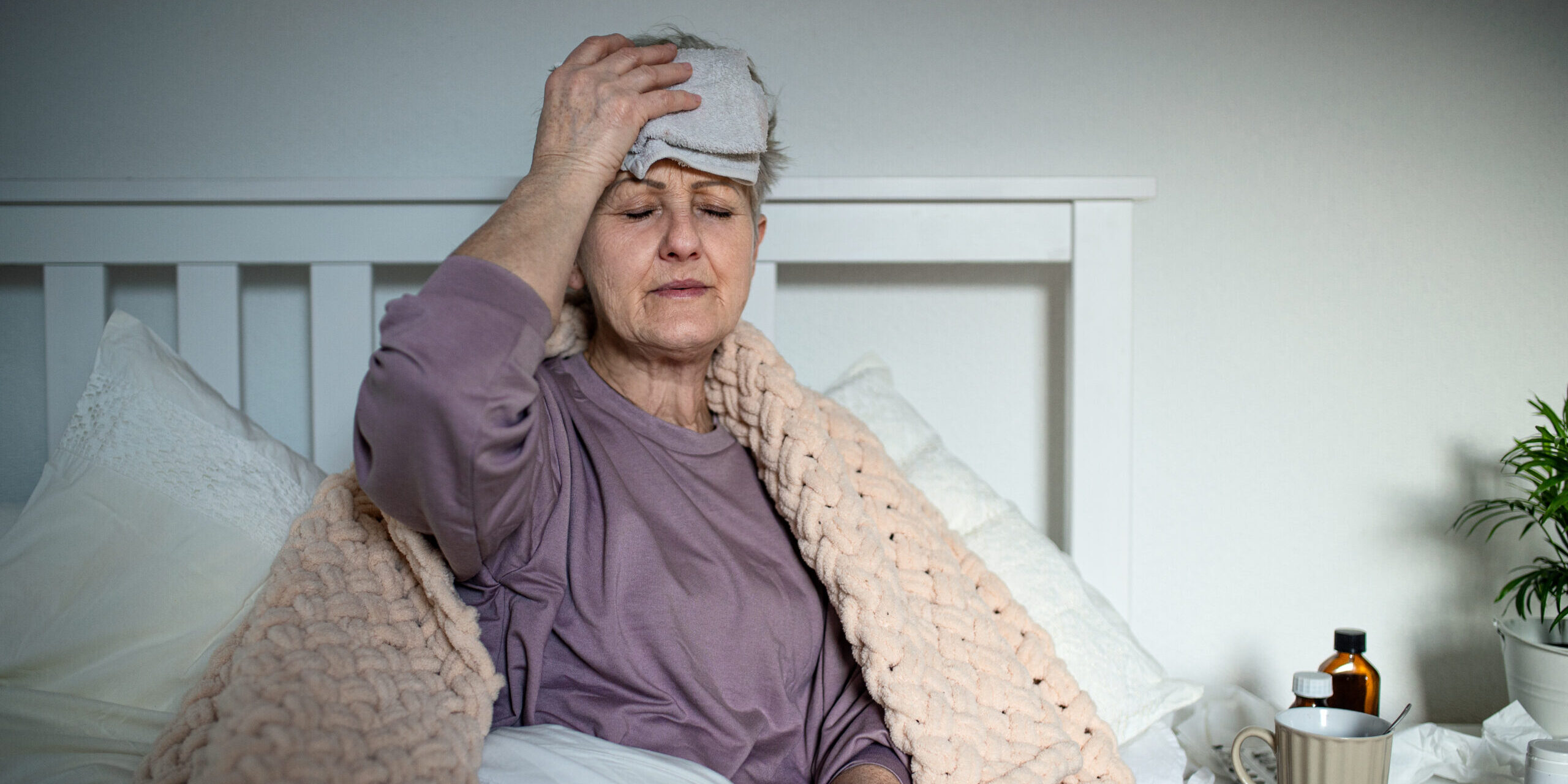 Sick senior woman with headache in bed at home, headache and side effects of vaccination effects.